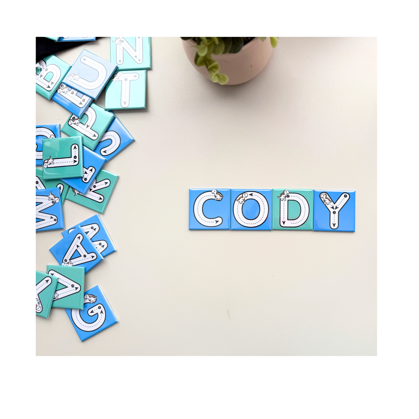 A set of four custom name tracing magnets spelling CODY. The magnets are blue and green with dashed tracing lines and dinosaur illustration for early learning. 