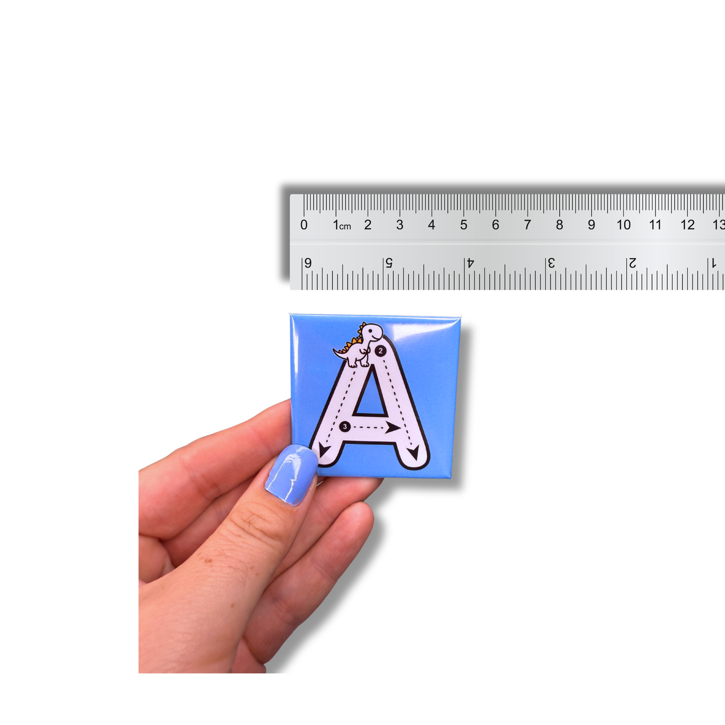 A hand holding a blue, 5cm (approx 2.36 inch) square alphabet tracing magnet next to a ruler, showing the exact product size and scale for early learning practice.