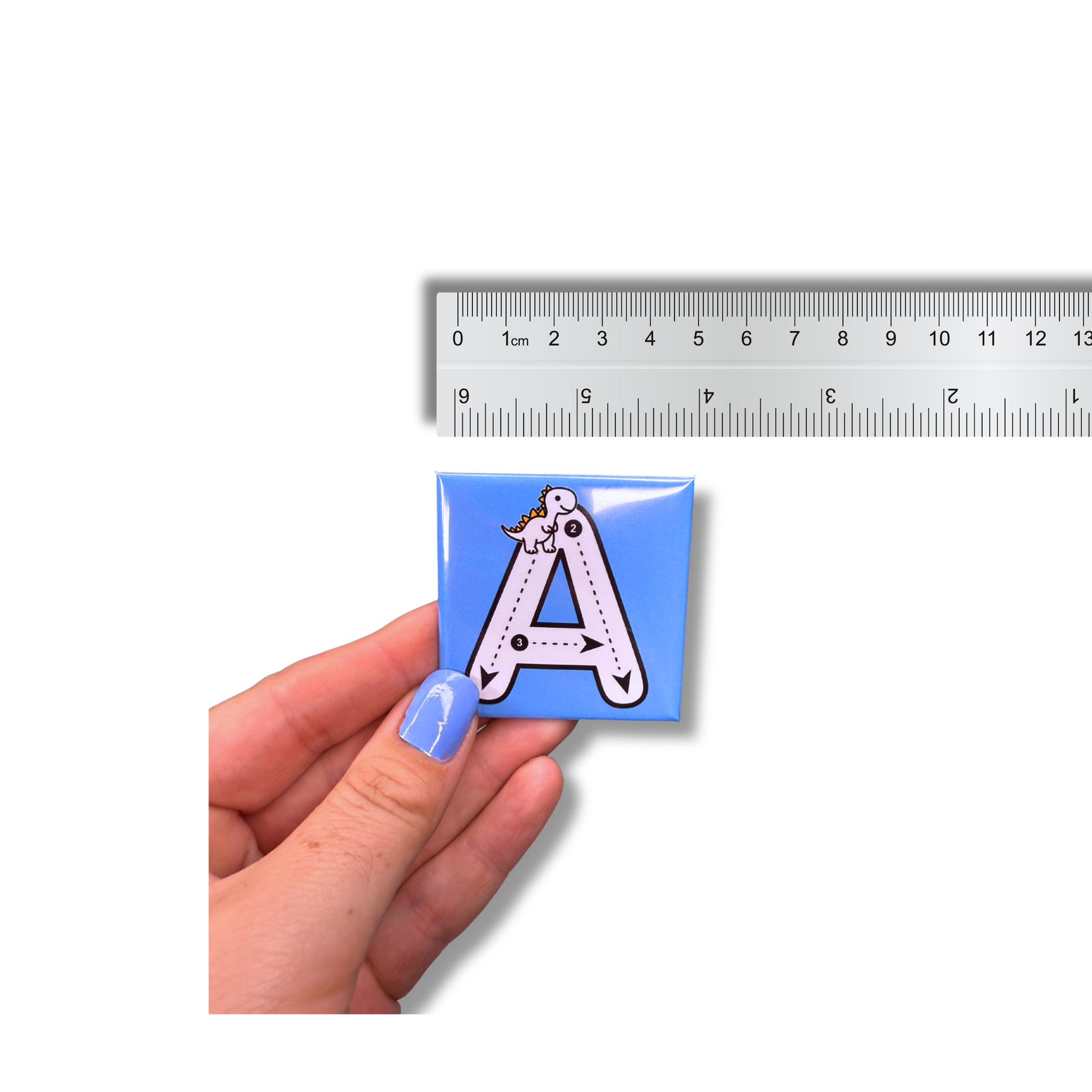 A hand holding a blue, 5cm (approx 2.36 inch) square alphabet tracing magnet next to a ruler, showing the exact product size and scale for early learning practice.