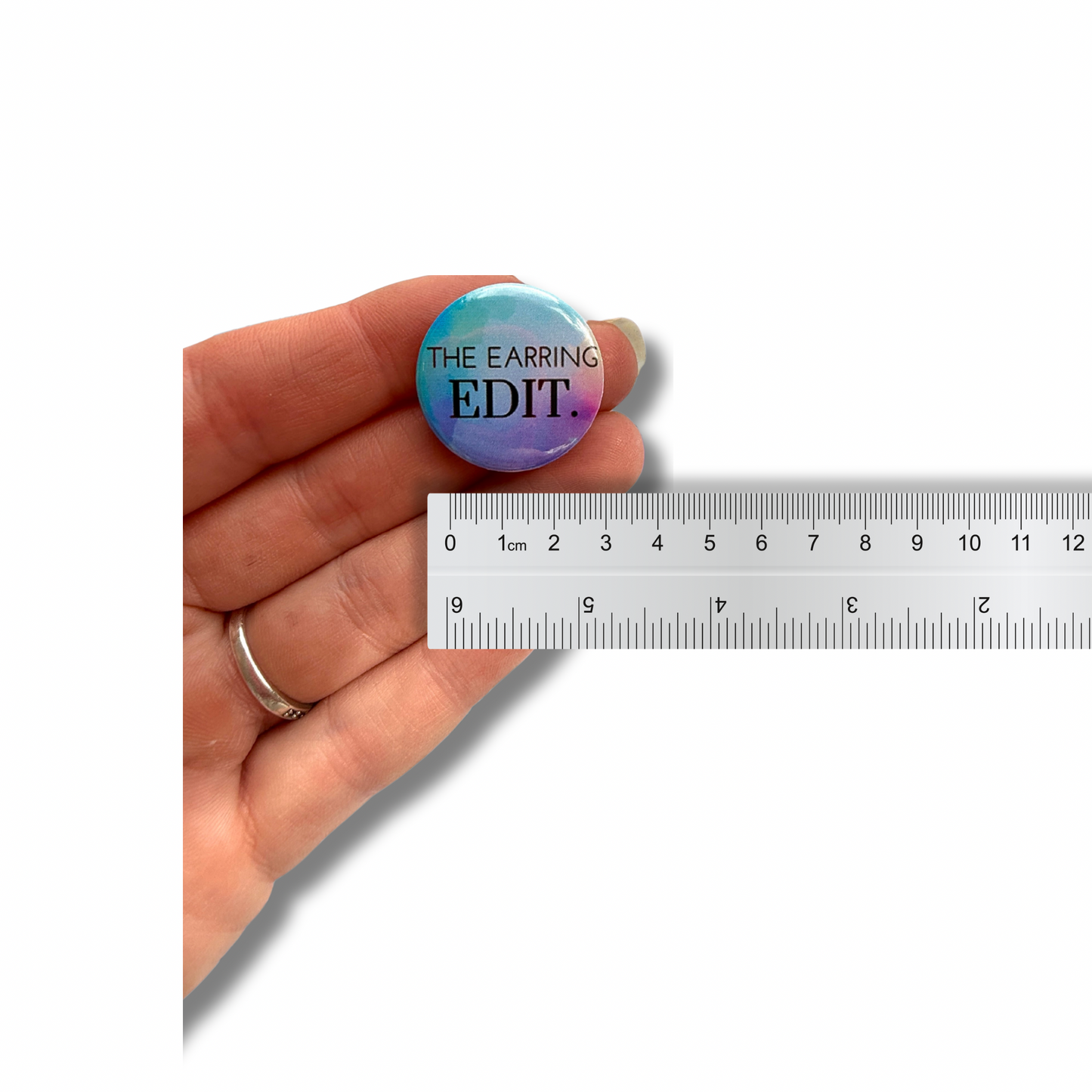 A hand holding one round custom logo magnet next to a ruler for accurate size and scale comparison.