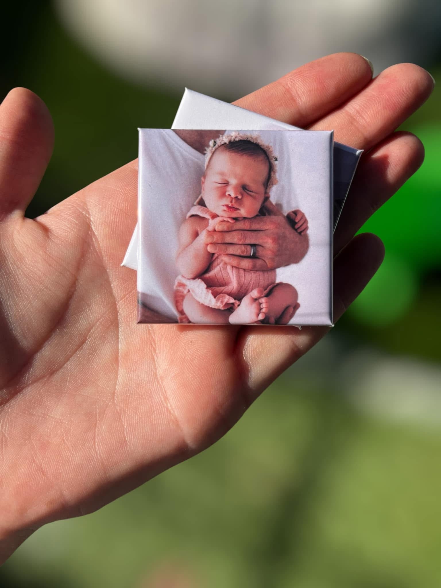 Custom photo magnet held in hand, featuring a sleeping newborn baby in pink outfit with floral headband – perfect for baby milestone gifts.
